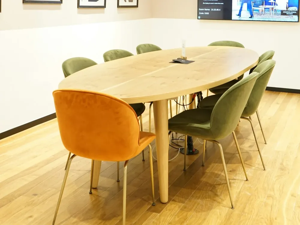 Konferensrum med ovalt träbord och stolar i grönt och orange